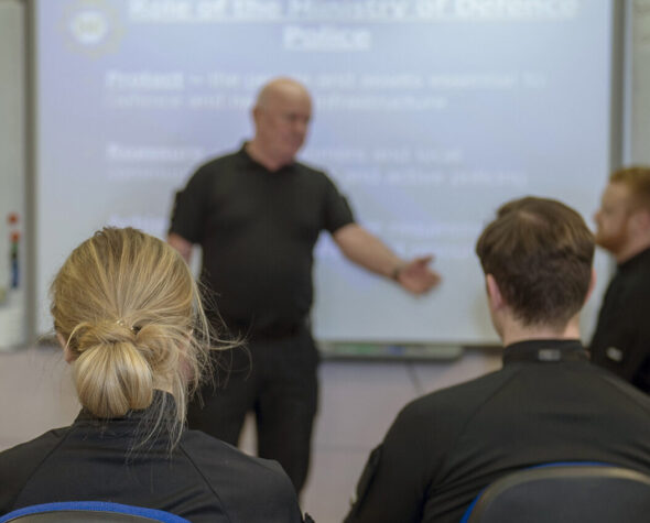 Ministry of Defence Police new recruits in a classroom in front of a whiteboard with a trainer delivering a lesson