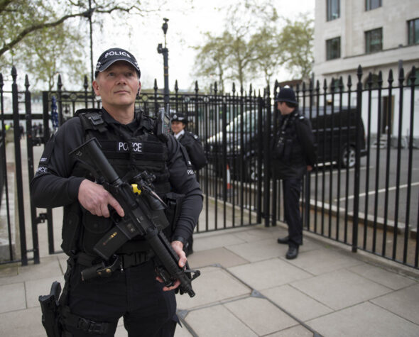 Ministry of Defence Police Officer in London holding a gun with officers behind him in a gated off area