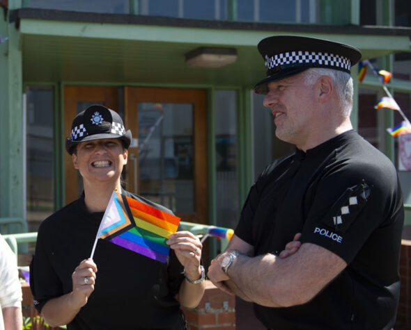 Two Ministry of Defence Police officers at a community event, with the female officer holding a pride flag